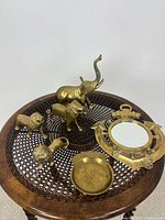 All items shown arranged on a round metal tray; includes 3 brass lion figurines, 1 brass elephant, brass dish, and nautical brass mirror.