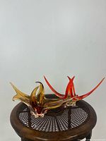 Pair of glass sculptures on wooden mesh stool, amber and red colors with original stickers, showcasing size and organic form