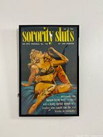 Framed pulp fiction poster titled "Sorority Sluts" showing a man and woman in an intimate scene in vintage style illustration.
