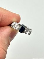 Ring held between fingers showing sapphire center and accent stones