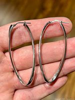 Both elongated sterling silver twisted hoop earrings held in hand
