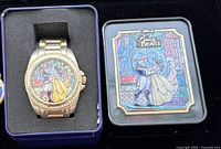 Watch in presentation box next to tin showing dial and artwork