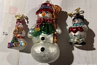 Three Radko snowman ornaments laid out: one large, two small