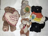 Four Boyds Bears including brown bear with heart pillow, gray bear, brown and white bear, and black bear in knitted sweater.