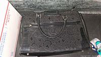 Top-down view of black purse showing floral pattern with some texture and handle details