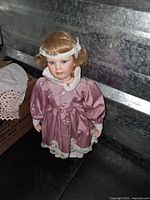 Front view of the blonde porcelain doll in pink satin dress with lace trim, showing facial features and hairstyle.