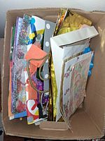 Multiple assorted gift bags inside a cardboard box showing various colors, patterns, and some bag handles visible including braided strings.