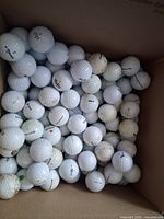 Box containing approximately 100 used golf balls, visible branding includes Titleist and others, condition ranges from lightly dirty to scuffed.