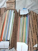 Two boxes filled with numerous assorted greeting cards and envelopes in upright organized stacks.