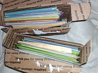 Card stacks arranged inside USPS Priority Mail boxes, showing layered colorful cards with envelopes