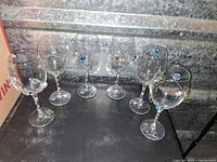 Full set of six clear glass wine glasses displayed together showing wire and bead decorations on each.