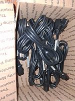 Box containing approximately 10 black power cords with NEMA 5-15P plugs and IEC C13 connectors.
