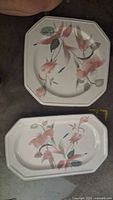 Top-down photo of two porcelain plates. One is square/octagonal with a pastel pink floral and green leaf design. The other is rectangular with similar floral decoration.