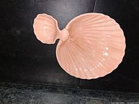 Large shell-shaped ceramic serving dish in light pink/peach color showing the detailed ridges and glossy finish