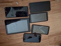 Six used cell phones lying on a wooden surface, screens visible but condition unclear, captured from front angle.