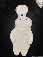 Front view of ceramic Pillsbury Doughboy kitchen decoration, white ceramic with blue eyes, nose, and buttons, chef's hat and scarf visible.