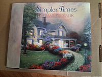 Cover of 'Simpler Times' showing a warmly lit house in an evening garden scene with colorful flowers and pathway.