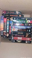 Photo showing 13 VHS tapes stacked in box with visible titles including The Edge, Star of Echoes, Untouchables, Subterano, and others.