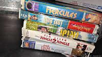 Side view of 5 clamshell VHS tapes stacked showing titles Hercules, The Love Bug, Jungle 2 Jungle, Far From Home, and Brother Bear.