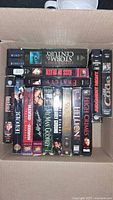 Top-down view of box with varying VHS tapes showing titles: Storm of the Century, Frailty, Kiss of Death, High Crimes, Judgment Night, Cradle among others.