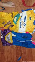 Photo of four cycling jerseys laid out on the floor, showing front sides and some details like logos and signatures