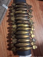 Set of 12 brass vintage drawer pull handles arranged on wooden floor, showing uniform design and size.