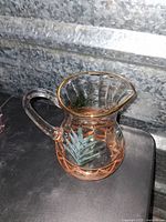 Front view of clear glass pitcher with green leaf hand painted design and gold trim around the rim and base. Shows handle and spout details.