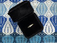 Ring in open black velvet jewelry box on blue patterned fabric