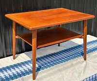 Angled view of the entire teak table showing top surface, lower shelf, and tapered legs