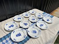 Twelve Royal Copenhagen Blue Flower dessert plates laid out on a cloth with a decorative runner.