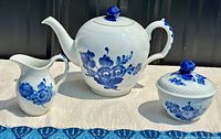 Full set of Royal Copenhagen Blue Flower pattern ironstone china including teapot, milk jug, and lidded sugar bowl shown on light cloth background