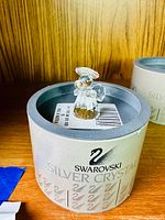 Swarovski Silver Crystal branded round box with angel figurine on shelf.