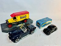 Vintage diecast yellow and red Champion Spark Plug delivery truck bank with dark blue convertible car and black VW Beetle Avon MIB on display.