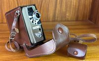 Vintage Eumig Electric Double 8 movie camera inside open brown leather carrying case with strap visible, camera angled facing forward showing lens and logo.