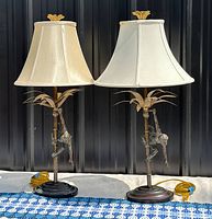 Two matching vintage gilt bronze table lamps side by side with off-white shades and yellow cords coiled at base.