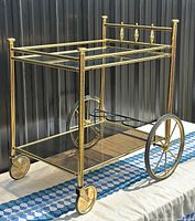 Three-quarter front view of the two-tier brass bar cart showing lucite shelves, large spoked wheels and small caster wheels.