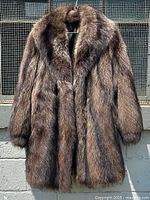 Full view of vintage raccoon fur coat hanging outdoors, showing natural brown fur with thick collar and long sleeves.