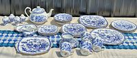Wide view of full set arranged outdoors on fabric with S&P shakers, sugar bowl, teapot, saucers, square plates, cookie platter, mugs, bowls and stacks of round plates