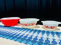 Three Pyrex mixing bowls arranged side by side on a surface: large solid red-orange, medium and small white with Friendship pattern.