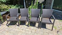 Four matching dark brown wicker patio armchairs on stone patio