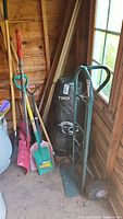 Group of hand truck, shovels, rake inside shed