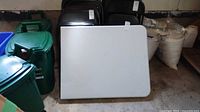 Folded white resin table leaning against wall near bins