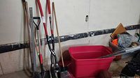 Group shot of all yard tools leaning against wall with tote