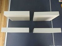 Four white rectangular floating shelves laid out on a black surface, top view showing thickness and edges.