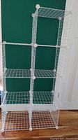 White wire storage shelving in front of a green wall and white door showing six compartments in a two-column arrangement, modular and adjustable design.