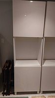 Tall white IKEA BESTA cabinet with two closed doors and open middle shelf section.