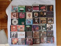 Full layout view of approximately 40 CDs arranged on a white surface, showing various album covers predominantly from the 70s and 80s.