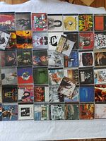 Top view of approximately 50 CDs laid out on white surface showing various album covers from 1990s music.