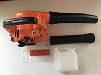 Leaf blower with two tube sections, tool kit bag, fuel bottle on table
