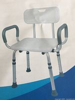 Stock photo of assembled shower chair showing seat, backrest, padded armrests, adjustable legs with rubber tips